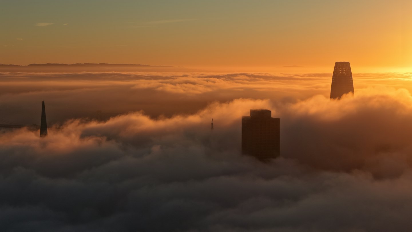 Business district towers rising above a sea of clouds at sunset
